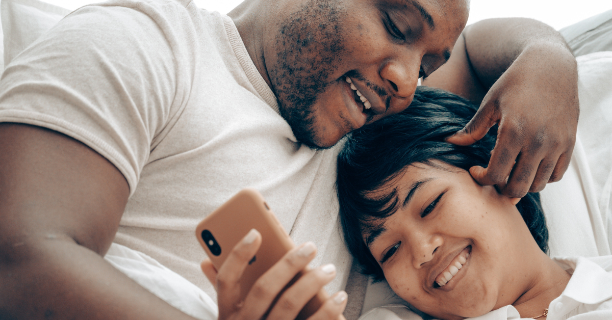 couple cuddling in bed looking at a smartphone