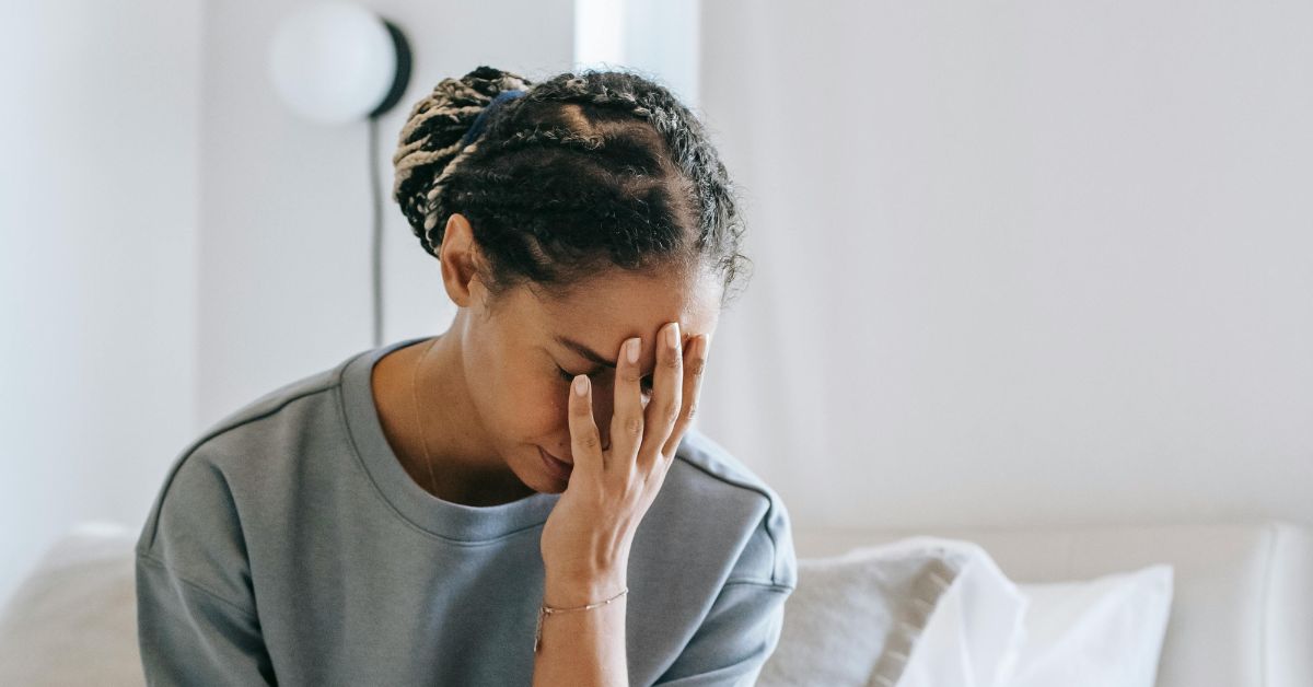 anxious black woman sitting on her bed covering her face with her hand